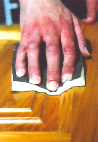 Photo of a person using a rawhide sanding pad on an uneven varnished wood surface